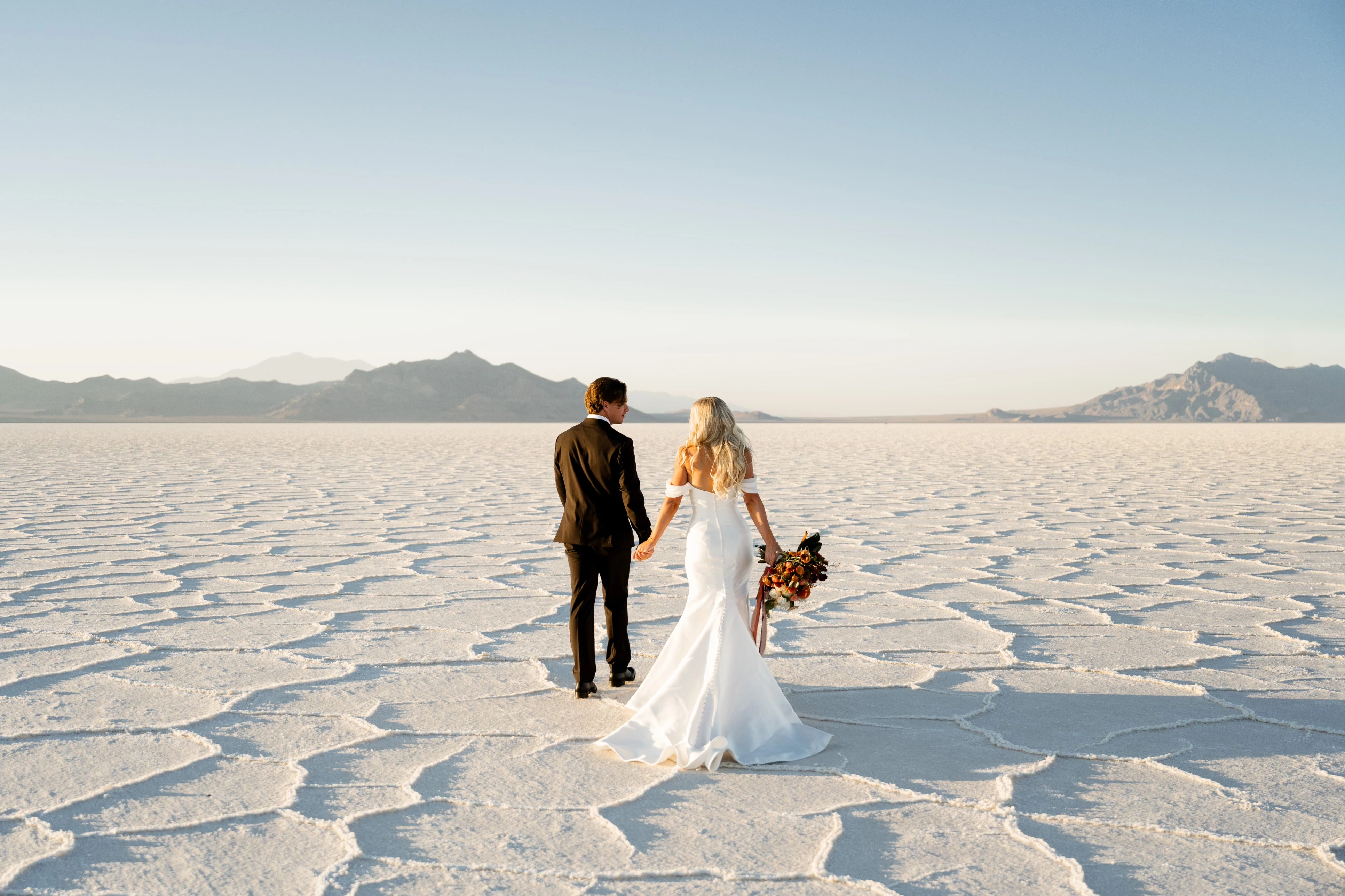 Bride wearing Pippa fit-and-flare wedding dress by Rebecca Ingram walking on the salt flats with her husband.